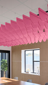 Pink scalloped acoustic baffle panels suspended from ceiling above wooden wall paneling in interior space.