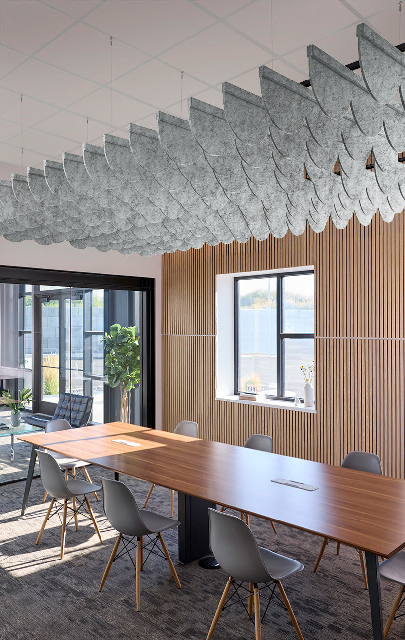 A modern conference room with a long wooden table, gray chairs, a slatted wood wall, and a large sculptural cloud-like pendant light hanging from the ceiling.