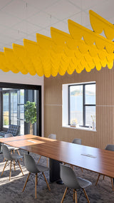 Bright yellow scallop-shaped acoustic baffle suspended from ceiling in modern office space above wooden conference table.