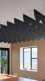 Black scallop-shaped acoustic baffle panels suspended from ceiling above wood-slat wall with window view.