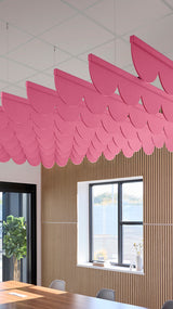 Pink scallop-shaped acoustic baffles suspended from ceiling above wooden wall paneling in an office space.