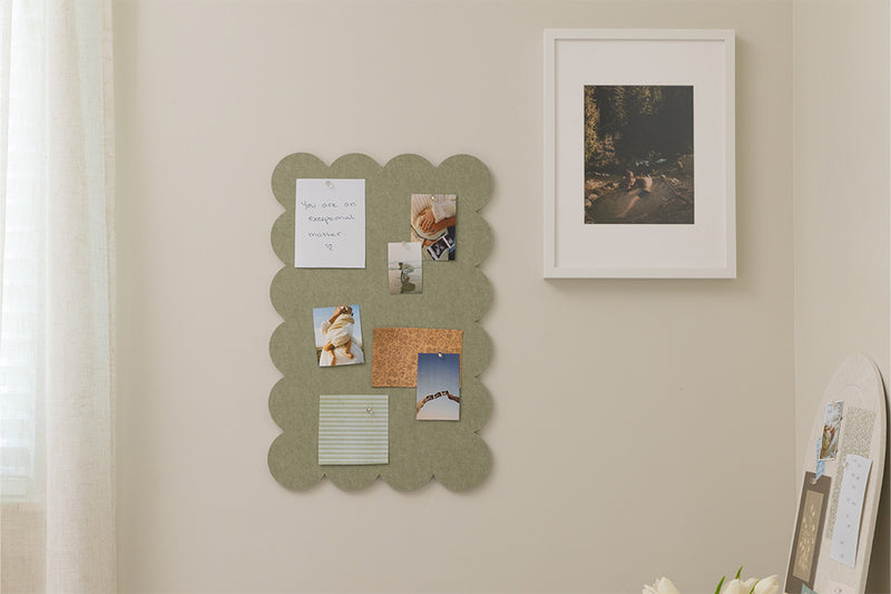 Scalloped green felt pinboard with photos and notes on a beige wall.