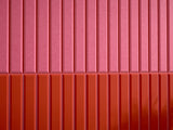 Two-toned corrugated metal surface with hot pink upper half and scarlet red lower half divided horizontally.