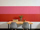 Large wall panels with vertical ribbed texture in layered hot pink and scarlet red colors behind wooden table and gray chairs