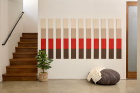 A Felt Right wall art design using browns, reds, and creams creating a pattern along a wall next to stairs and a house plant.