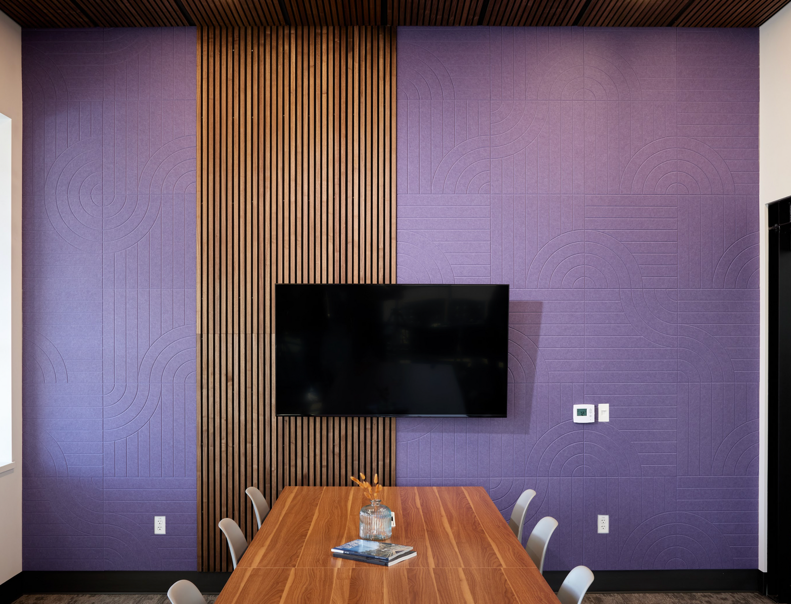 A Felt Right Wall design in a purple shade used in a conference room with a tv and wood in front of a conference table for an office or board room.