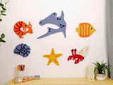 Six felt sea animal cutouts including orange fish, blue stingray, yellow striped fish, shell, starfish, and red shrimp.