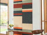 Colorful geometric wall panel in a room with a window and wooden chair.