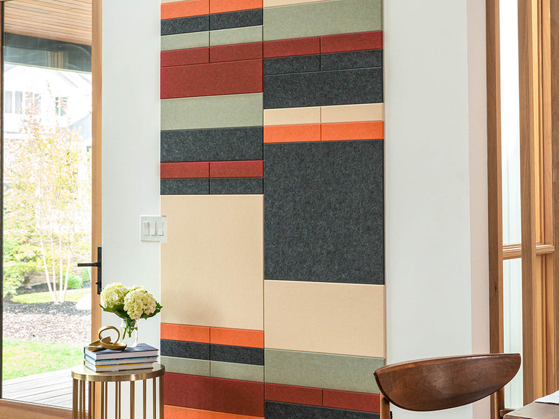 Colorful geometric wall panel in a room with a window and wooden chair.
