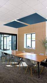 Two dark teal square acoustic panels suspended from white ceiling grid above conference table in office space.