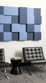 Three-dimensional acoustic wall panels in light and dark blue arranged in a grid pattern above modern black leather seating.
