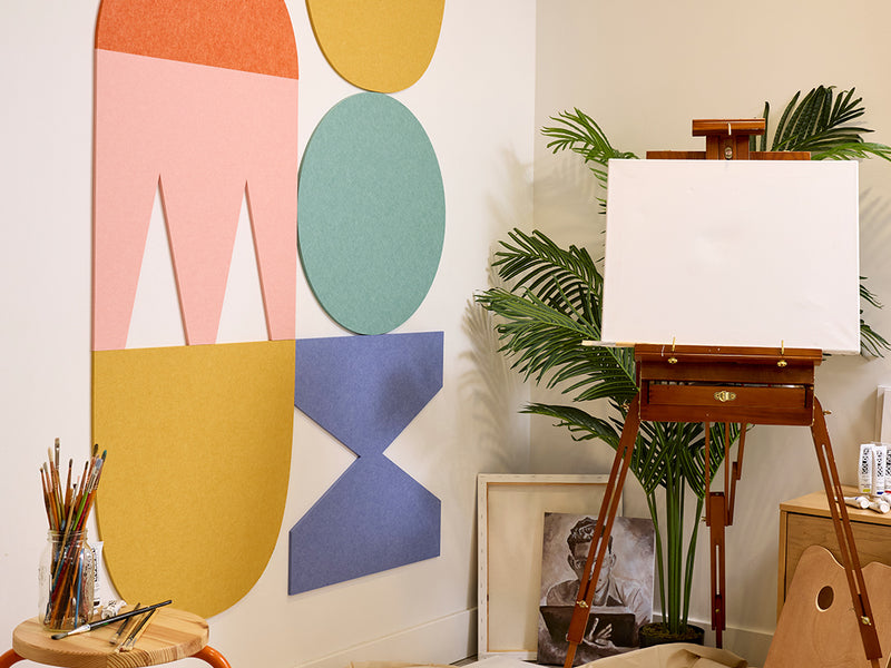 Art studio with a white canvas on an easel, colorful abstract wall art, and plants.