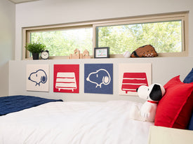 Bedroom with Snoopy plush toy and decorative pillows on a bed, featuring Snoopy illustrations on the wall.