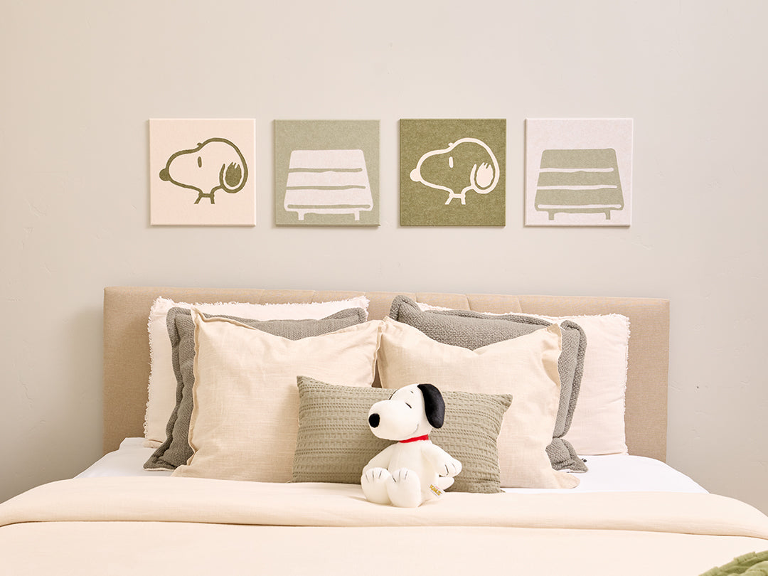 Bedroom with Snoopy plush toy and decorative pillows on a bed, featuring Snoopy illustrations on the wall.