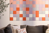 Rectangular wall art with colored squares in orange, pink, purple, and gray tones hung above a dark sofa.