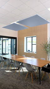 Two blue-gray flat square acoustic baffles suspended from ceiling above conference table in office space.