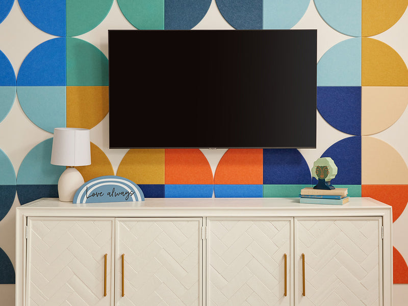 A Felt Right wall art design using quarter circles in shades of blue, orange, yellow, and cream to make  a back drop behind a tv and a tv stand.