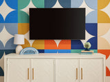 A Felt Right wall art design using quarter circles in shades of blue, orange, yellow, and cream to make  a back drop behind a tv and a tv stand.