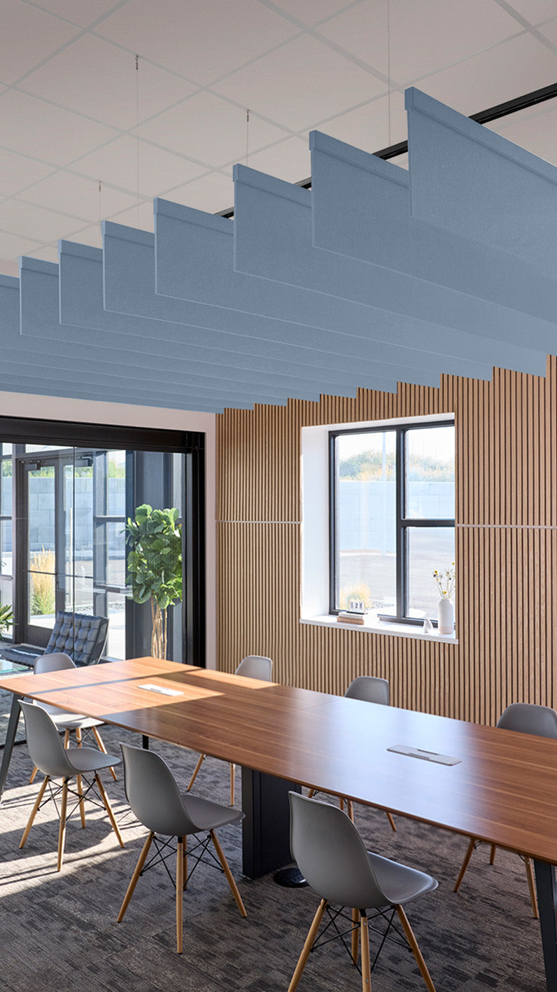 Blue-gray acoustic baffles suspended from ceiling in office conference room with wooden table and chairs.