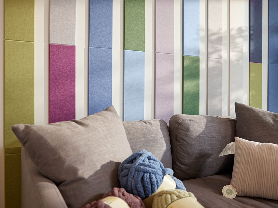 Felt right wall art design in shades of blue, green, purple, and cream felt tiles in a geometric shape lining the wall and the ceiling in a living room with a couch and some yarn.