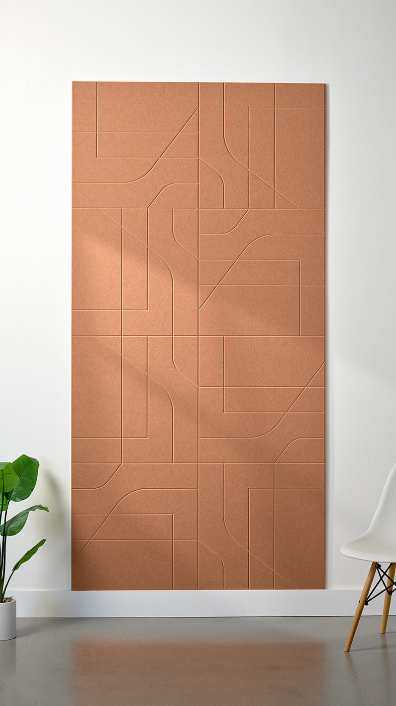 Light orange Felt Right 4’ x 8’ PET felt panel with intersecting lines similar to a transit system map engraved into the material against a white wall. A plant and chair are in the foreground.