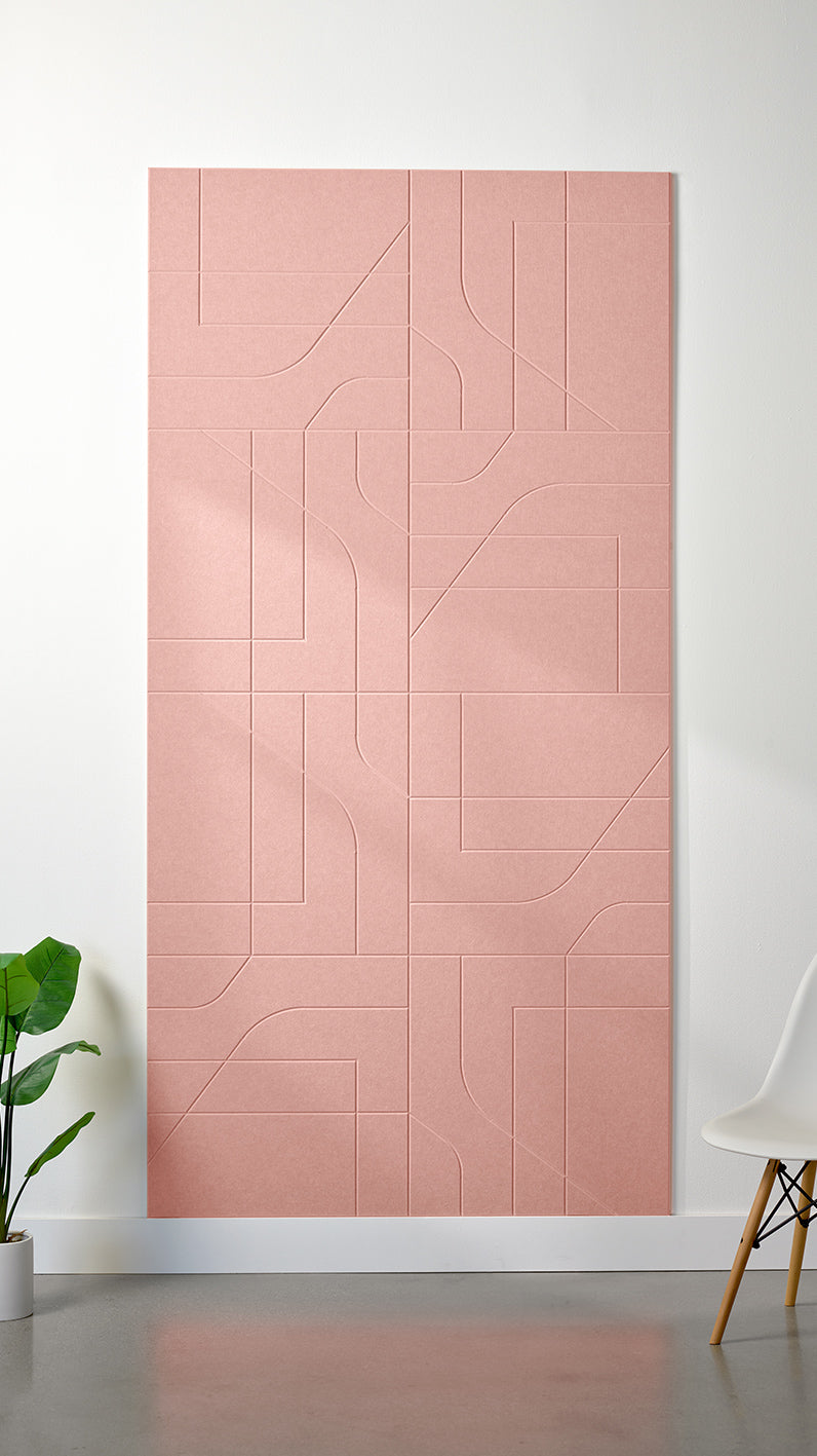 Light pink Felt Right 4’ x 8’ PET felt panel with intersecting lines similar to a transit system map engraved into the material against a white wall. A plant and chair are in the foreground.
