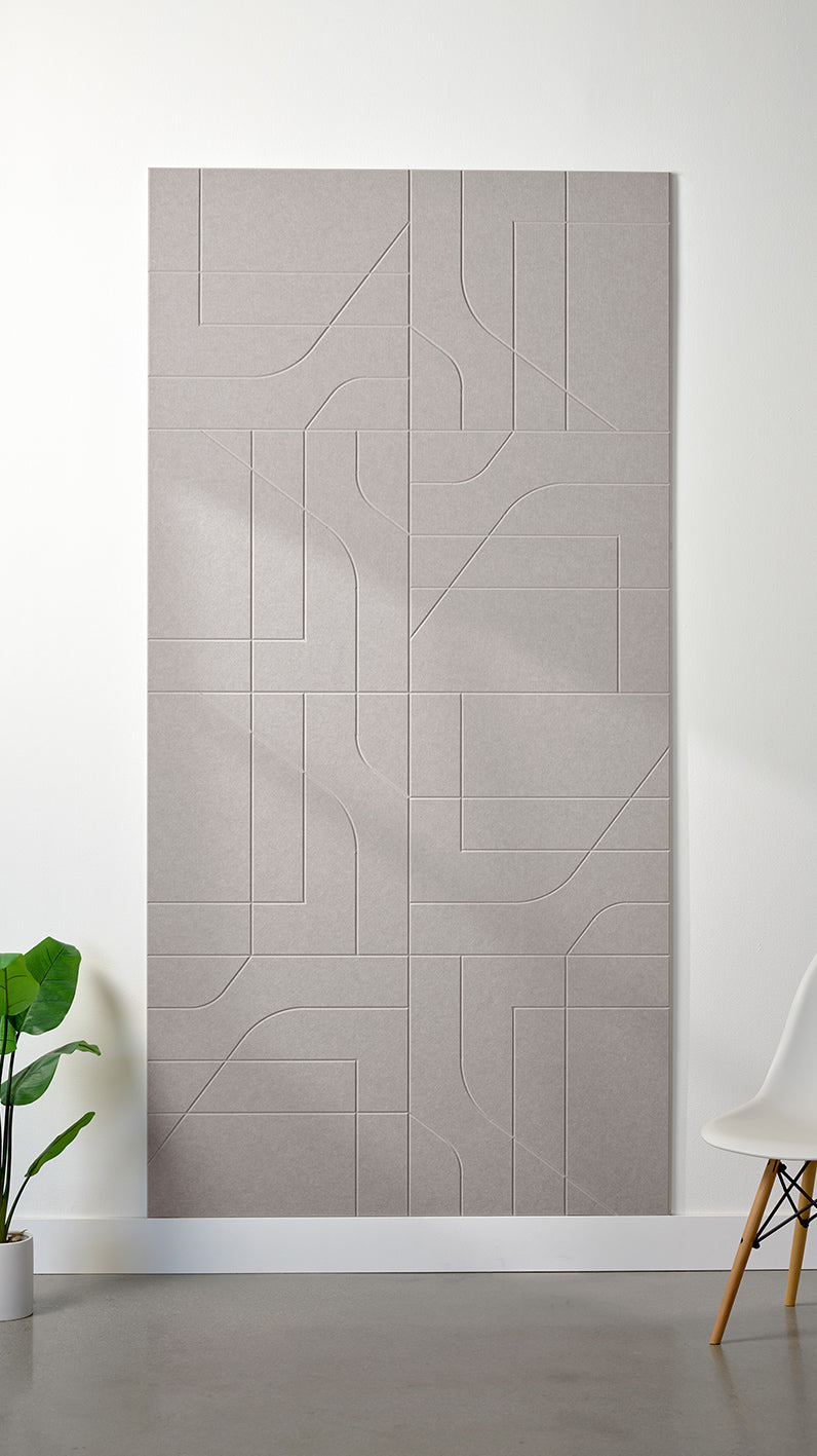 Light grey Felt Right 4’ x 8’ PET felt panel with intersecting lines similar to a transit system map engraved into the material against a white wall. A plant and chair are in the foreground.