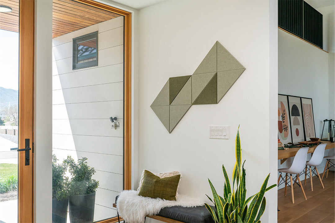 A Felt Right wall art design in shades of green creating a switchback pattern on a wall above a bench and a house plant and a window.
