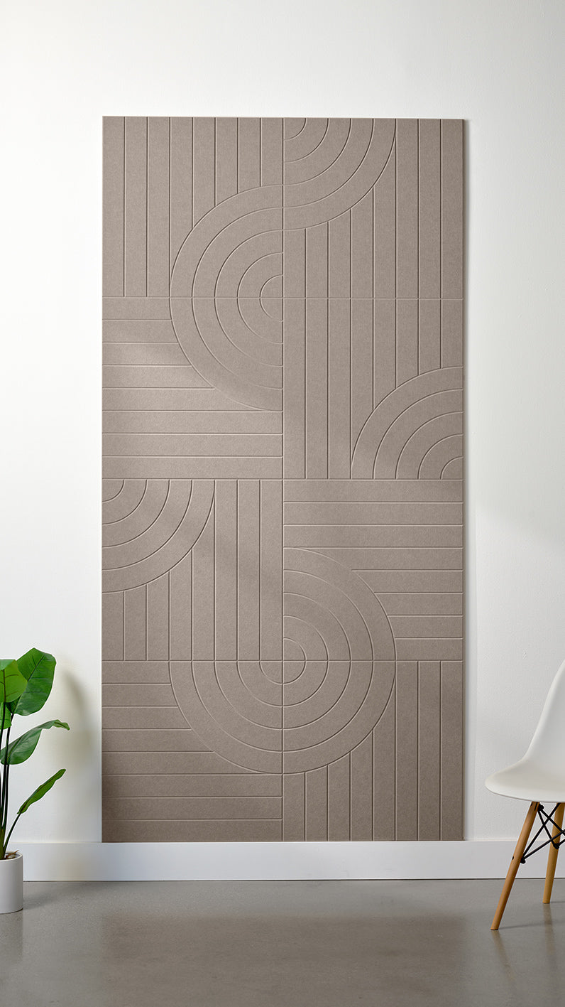 Greyish beige Felt Right 4’ x 8’ PET felt panel with straight and circular lines engraved into the material against a white wall. A plant and chair are in the foreground.