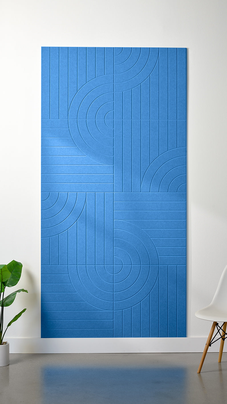 Blue Felt Right 4’ x 8’ PET felt panel with straight and circular lines engraved into the material against a white wall. A plant and chair are in the foreground.