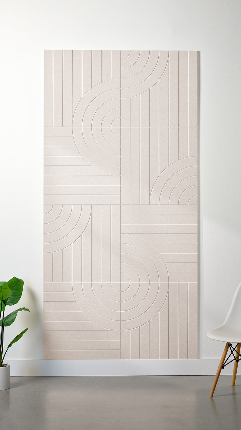 Heathered beige Felt Right 4’ x 8’ PET felt panel with straight and circular lines engraved into the material against a white wall. A plant and chair are in the foreground.