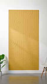 Mustard yellow Felt Right 4’ x 8’ PET felt panel with straight and circular lines engraved into the material against a white wall. A plant and chair are in the foreground.