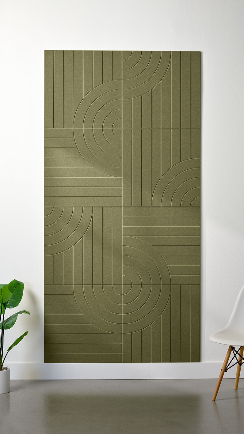 Olive green Felt Right 4’ x 8’ PET felt panel with straight and circular lines engraved into the material against a white wall. A plant and chair are in the foreground.