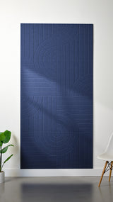 Dark blue Felt Right 4’ x 8’ PET felt panel with straight and circular lines engraved into the material against a white wall. A plant and chair are in the foreground.