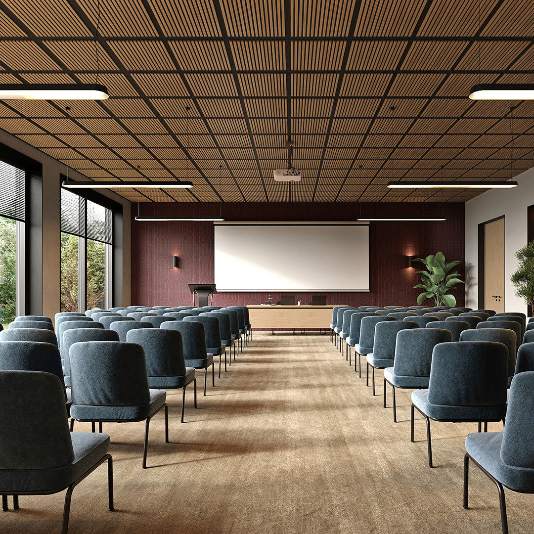 A large conference room with rows of blue-gray upholstered chairs facing a white projection screen, set in a modern interior with a slatted wood ceiling, warm wood floor, and large windows on the side.