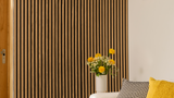 Decorative wall with vertical slats, a vase of yellow flowers on a table, and a yellow cushion.