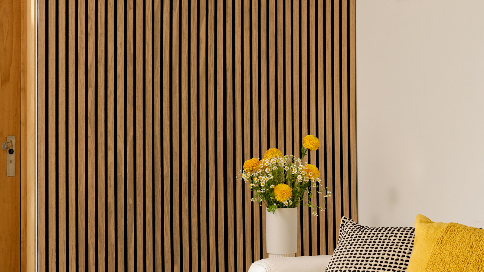 Decorative wall with vertical slats, a vase of yellow flowers on a table, and a yellow cushion.