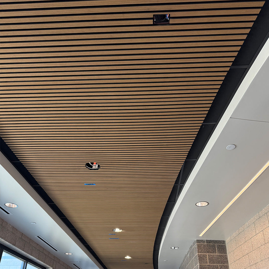 Wood slat ceiling panels installed in a modern indoor space, shown from an upward angle with recessed lighting and architectural trim visible.