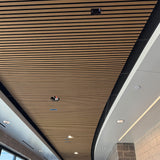 Wood slat ceiling panels installed in a modern indoor space, shown from an upward angle with recessed lighting and architectural trim visible.