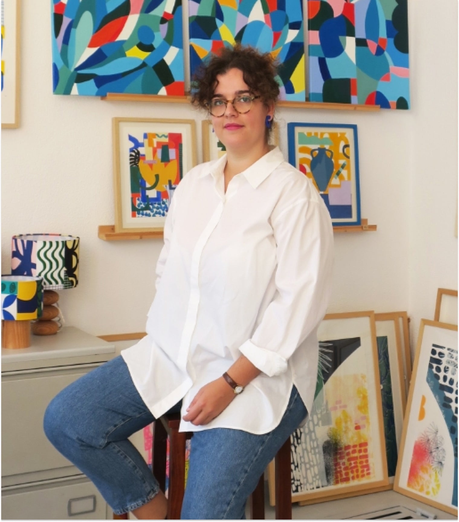 Designer Teresa Rego sitting in an art studio with colorful abstract paintings on the wall.