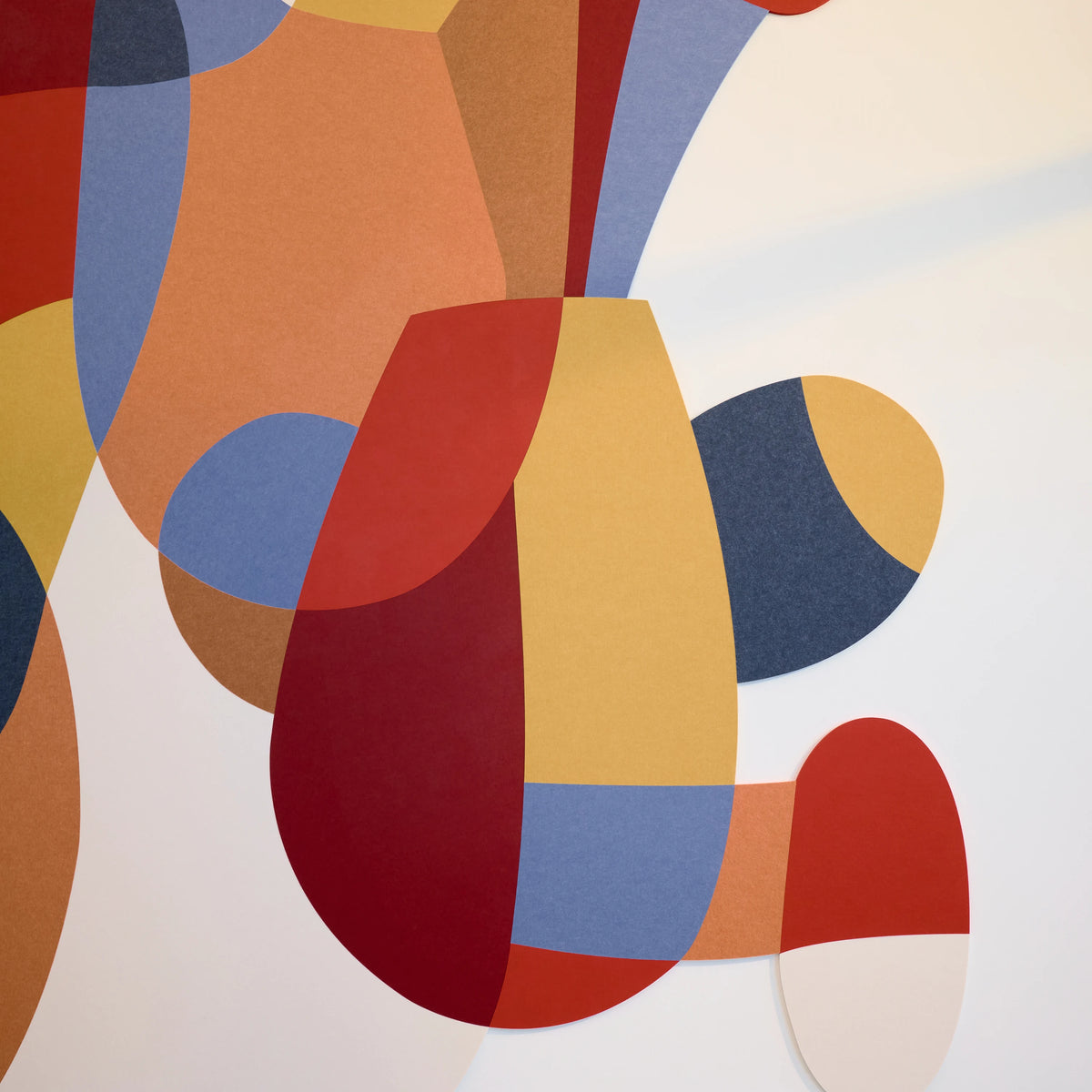 Abstract geometric wall art featuring overlapping organic shapes in terracotta red, mustard yellow, slate blue, tan, and cream on a white background.