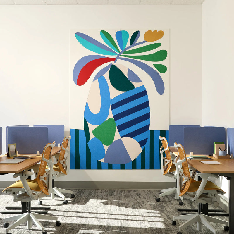 Large abstract wall art featuring bold tropical leaves and organic shapes in blue, green, teal, red, cream, and yellow, displayed in a modern office setting above desks and ergonomic chairs.