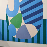 Abstract geometric wall art featuring overlapping organic shapes and stripes in blue, navy, green, cream, and muted lavender, photographed against a white wall.