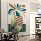 A large abstract wall art print featuring a stylized tropical leaf motif in teal, green, cream, orange, and light blue, displayed on a white wall in a modern office interior with a meeting table, chairs, and shelving visible.