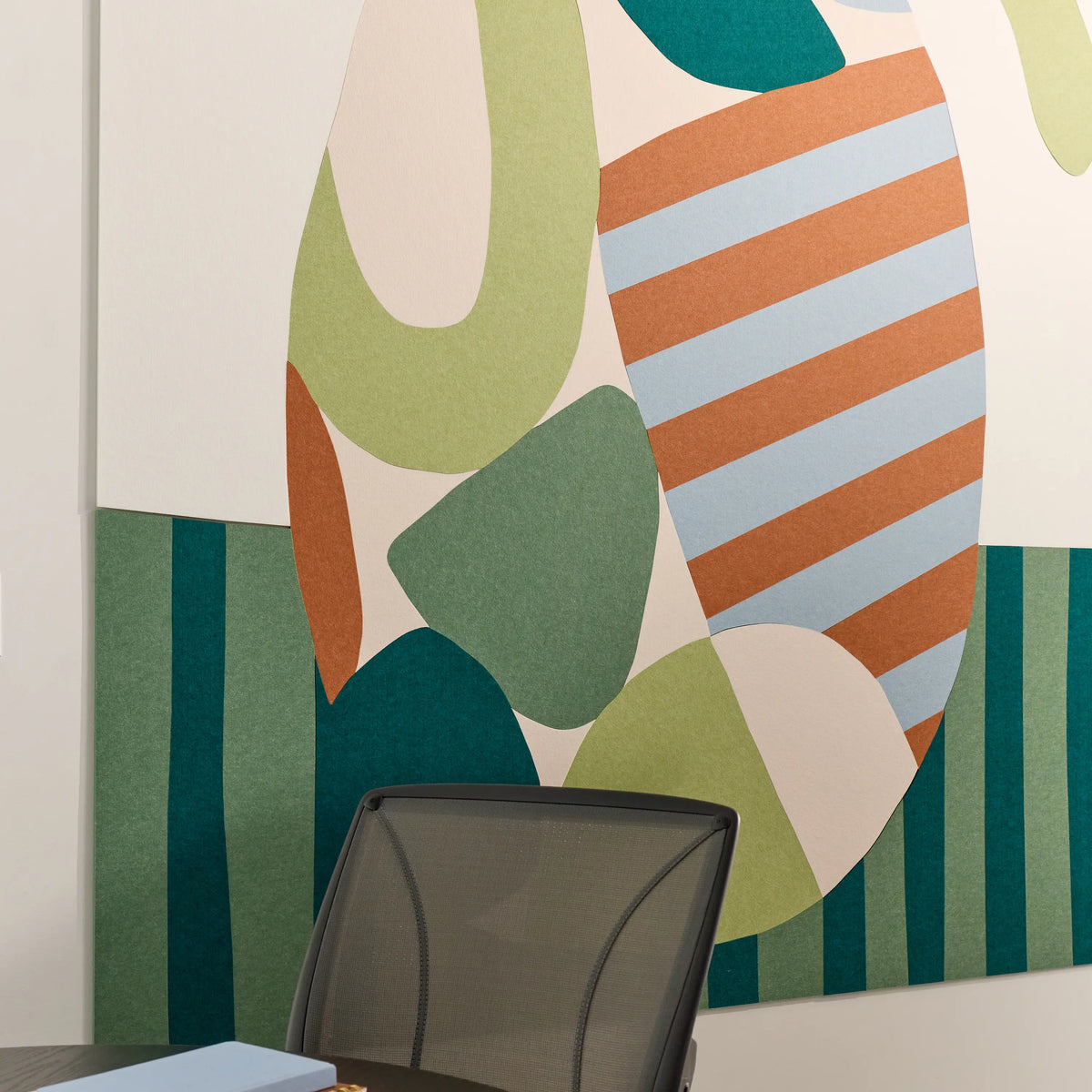 Abstract geometric wall art with overlapping organic shapes and striped sections in sage green, teal, rust orange, light blue, and cream, shown hanging above a dark office chair.