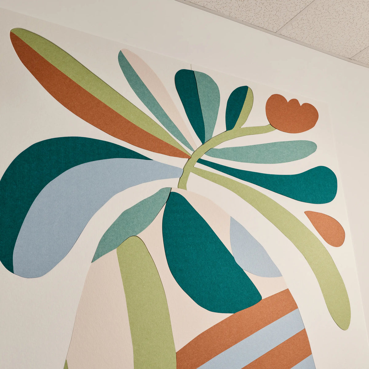 Abstract botanical wall art featuring layered organic leaf shapes in teal, sage green, light blue, terracotta, and cream on a white wall.
