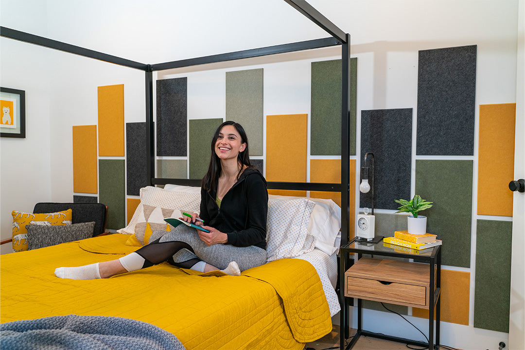 A Felt Right wall design in yellow, green, and grey behind a bed and a side table with a look of a headboard using big rectangles.
