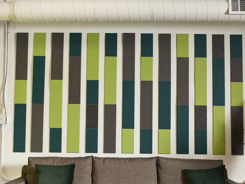 A Felt Right wall art design in shades of grey and green above a couch on the wall in a stripe like pattern 