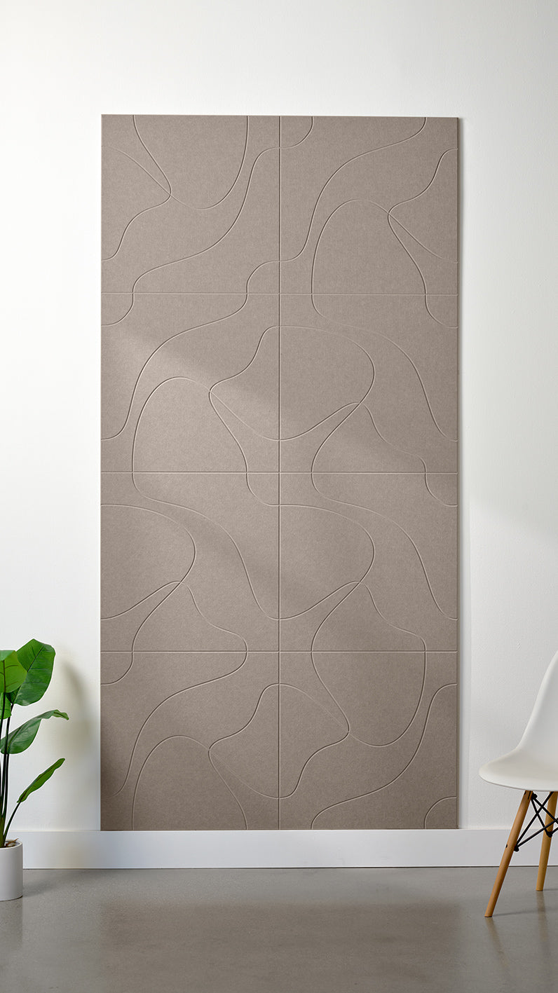 Greyish beige Felt Right 4’ x 8’ PET felt panel with flowing lines similar to a topographical map engraved into the material against a white wall. A plant and chair are in the foreground.