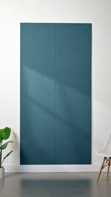 Dark blue Felt Right 4’ x 8’ PET felt panel with flowing lines similar to a topographical map engraved into the material against a white wall. A plant and chair are in the foreground.
